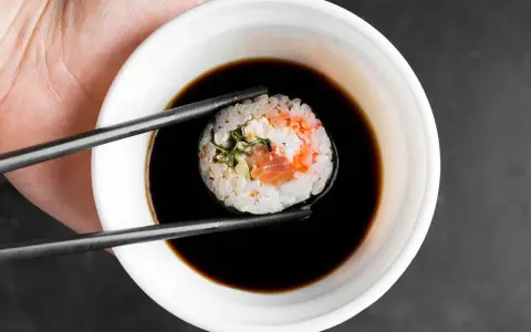 Pałeczkami zanurzam sushi w sosie do sajgonek. Widać kawałek łososia i ryż.