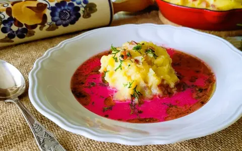 Pyszny barszcz czerwony zabielany, przepis babci. Na talerzu purée ziemniaczane z boczkiem i koperkiem w intensywnym, różowym barszczu.