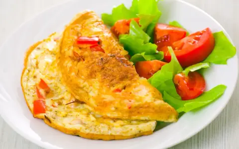 Złocisty omlet francuski z kawałkami papryki, podany z sałatką z pomidorów i sałaty. Pyszne śniadanie.