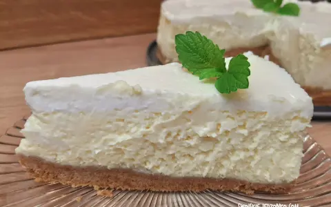 Pyszny sernik z bitą śmietaną siostry Anastazji, udekorowany listkiem mięty, na szklanym talerzu.