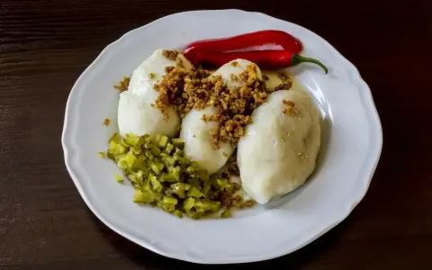 Trzy ziemniaczane kartacze z okrasą, posypane skwarkami, podane z ogórkiem kiszonym i papryczką chili.