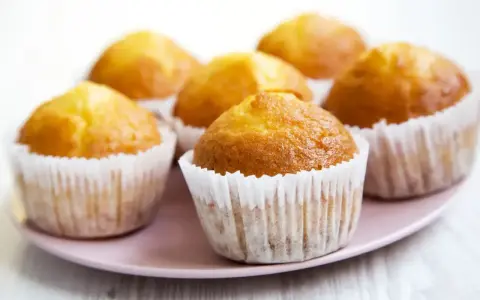 Idealny przepis na wilgotne i puszyste muffinki. Złociste, pachnące babeczki na różowym talerzyku.