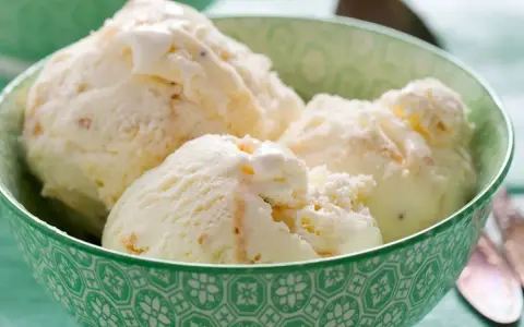 Puszyste lody z mascarpone, pełne delikatnych kawałków, kuszą kremową konsystencją w zielonej miseczce.
