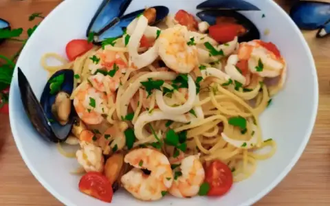 Pyszne linguini z krewetkami, kalmarami i małżami, ozdobione pomidorkami i natką pietruszki.