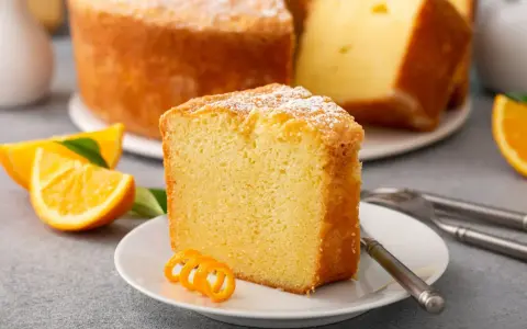 Wilgotna babka cytrynowa, posypana cukrem pudrem, z plasterkami pomarańczy i ozdobną skórką. Idealna na deser.