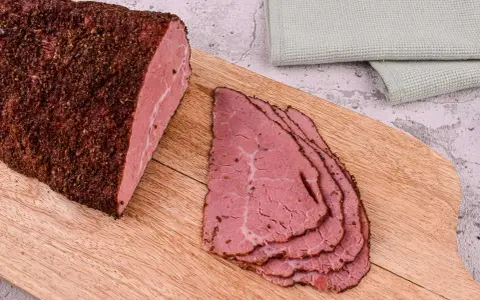Kawałek pastrami, co to jest? Aromatyczne, peklowane i wędzone mięso wołowe, pokrojone w cienkie plastry, leży na desce.