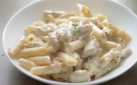 Penne z kurczakiem w kremowym sosie śmietanowo-serowym, udekorowane gałązką ziół. Pyszne danie obiadowe.
