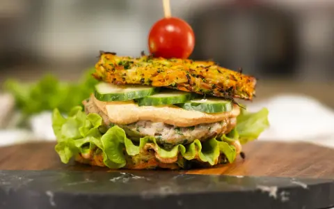 Burger z warzywną bułką, kotletem, ogórkiem, sosem i pomidorkiem na wykałaczce.