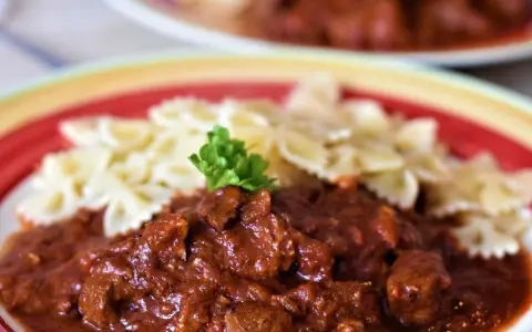 Gulasz z indyka z warzywami, podany z makaronem w kształcie motylków, ozdobiony natką pietruszki. Pyszne danie na talerzu.