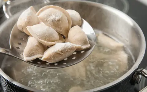 Gotowanie pierogów: na łyżce cedzakowej świeżo uformowane pierogi czekają na wrzucenie do wrzątku.
