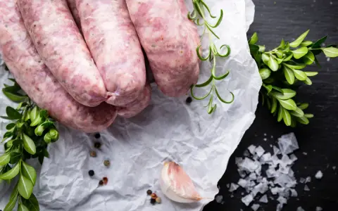 Surowa biała kiełbasa na papierze, obok gałązki rozmarynu i czosnek. Zastanawiasz się nad biała kiełbasa kcal?