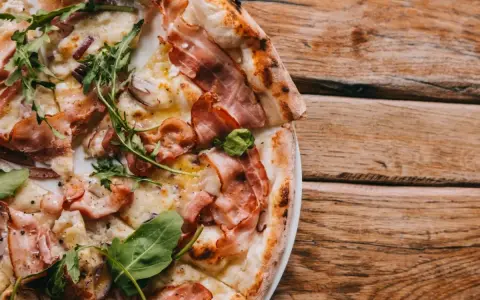 Pyszna pizza carbonara z chrupiącym boczkiem, rukolą i cebulą na drewnianym stole.