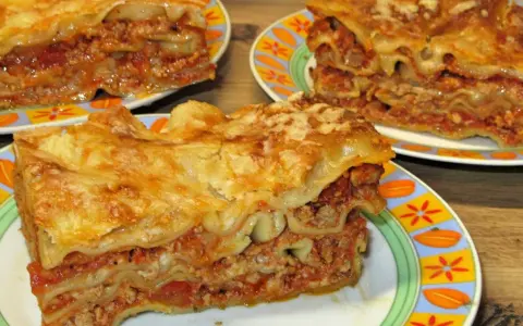 Prosty przepis na lasagne z mięsem mielonym. Aromatyczne, warstwowe danie z makaronem, sosem mięsnym i serem, podane na kolorowych talerzach.