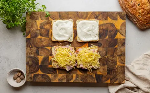 Przygotowanie croque madame: na kromkach chleba szynka i ser, na drugiej sos beszamelowy.