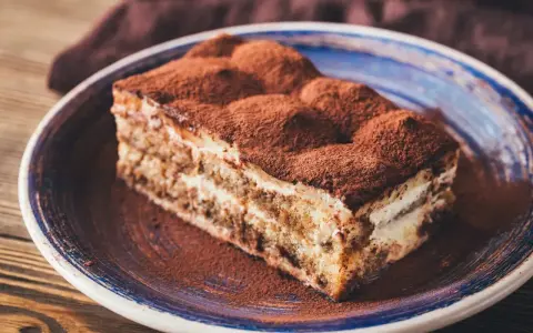 Pyszny kawałek tiramisu z mascarpone, posypany kakao, na niebieskim talerzu. Idealny na deser.
