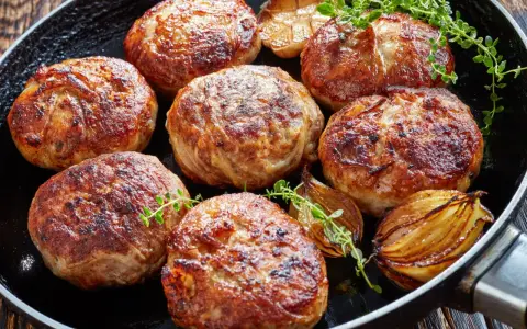 Usmażone kotlety na burgera z cebulą i ziołami na patelni.