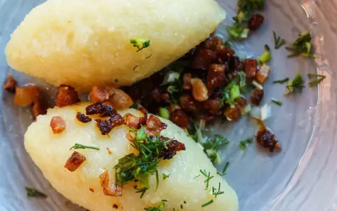 Dwa pyszne cepeliny z ziemniaków, polane skwarkami i posypane szczypiorkiem, wyglądają apetycznie.