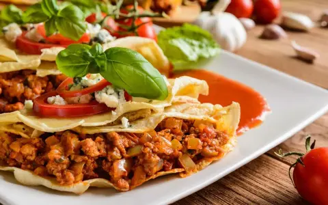 Pyszna tortilla z mięsem mielonym, polana sosem pomidorowym, ozdobiona bazylią i serem pleśniowym.