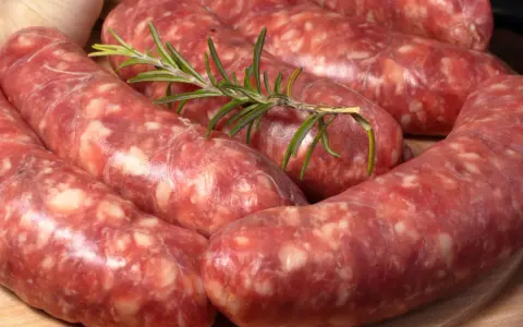 Salsiccia co to? Surowe kiełbaski wieprzowe, przyprawione ziołami, leżą na desce.