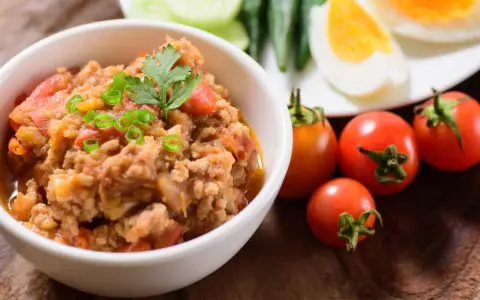 Pyszna pasta z makreli w pomidorach, udekorowana szczypiorkiem i natką. Obok świeże pomidorki i jajka na twardo.