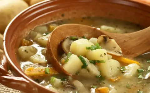 Gęsta zupa ziemniaczana z grzybami i marchewką, jak z przepisu babci. Drewniana łyżka zanurzona w aromatycznym bulionie.