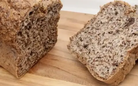 Chleb z siemienia lnianego, pokrojony na desce. Widoczny bochenek i dwa kromki, pełne ziaren.