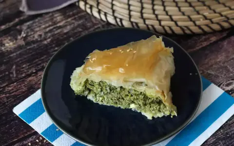 Kawałek spanakopity z chrupiącym ciastem filo i zielonym nadzieniem ze szpinaku i sera feta, posypany sezamem.