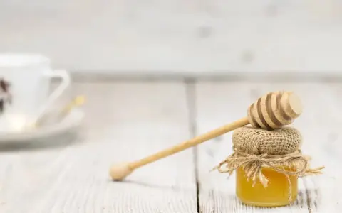 Mały słoiczek miodu z drewnianą chochlą, idealny do herbaty. Warto pamiętać o jego miód kcal.