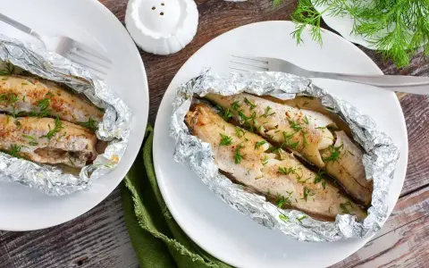 Dwa porcje soczystego mintaja z piekarnika, zapieczonego w folii aluminiowej, posypane świeżym koperkiem.