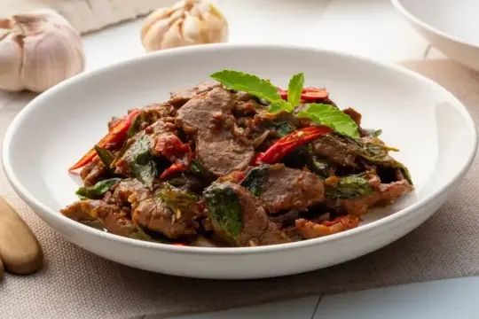 Aksamitne kawałki wołowiny po tajsku z bazylią i papryczką chili, podane w białej misce.