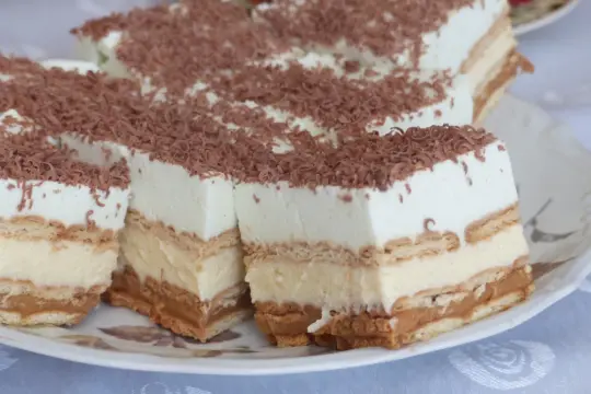Szybkie ciasto bez pieczenia z budyniem i herbatnikami, udekorowane wiórkami czekolady. Idealne na deser!