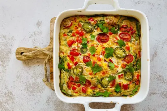 Pyszny omlet z piekarnika z pomidorkami, papryką i jalapeño, udekorowany natką pietruszki.