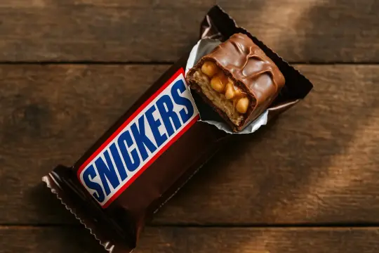 Czekoladowy batonik Snickers, częściowo wyjęty z opakowania, z widocznym nadzieniem z orzeszków ziemnych i karmelu. Idealny na szybką przekąskę, gdy liczą się snickers kcal.