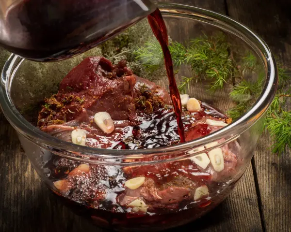 Ciemny płyn wlewa się do szklanej miski z karczkiem, czosnkiem i ziołami. Powstaje aromatyczna marynata do karczku.