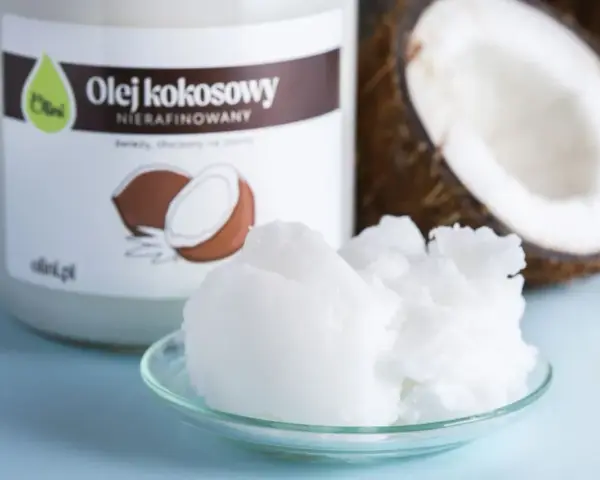 Olej kokosowy nierafinowany, idealny jako zdrowy olej do smażenia. W tle widać połówkę kokosa i słoik z etykietą.