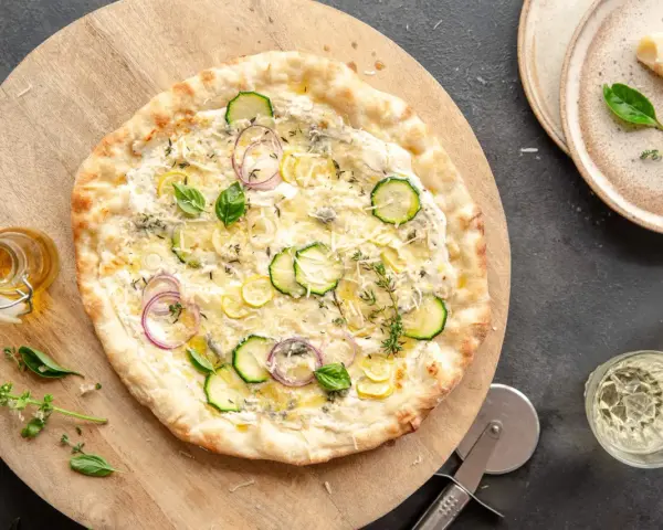 Pyszna pizza bianca z cukinią, cebulą i cytryną, ozdobiona bazylią i tymiankiem. Idealna na letni wieczór.
