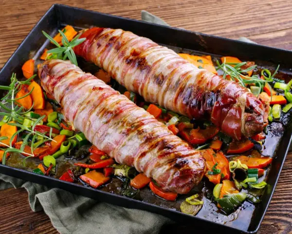 Pieczone polędwiczki wieprzowe w boczku, podane z pieczonymi warzywami i rozmarynem. Pyszna okrasa na obiad.