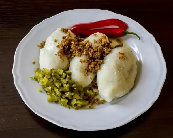 Trzy ziemniaczane kartacze z okrasą, posypane skwarkami, podane z ogórkiem kiszonym i papryczką chili.