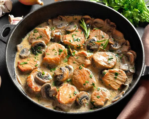 Soczysty schab w sosie pieczarkowym, udekorowany natką pietruszki, podany w żeliwnej patelni. Aromatyczne danie, które zachwyca smakiem.