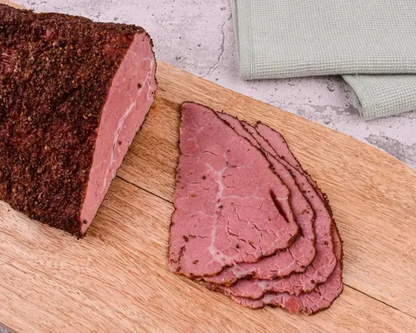 Kawałek pastrami, co to jest? Aromatyczne, peklowane i wędzone mięso wołowe, pokrojone w cienkie plastry, leży na desce.