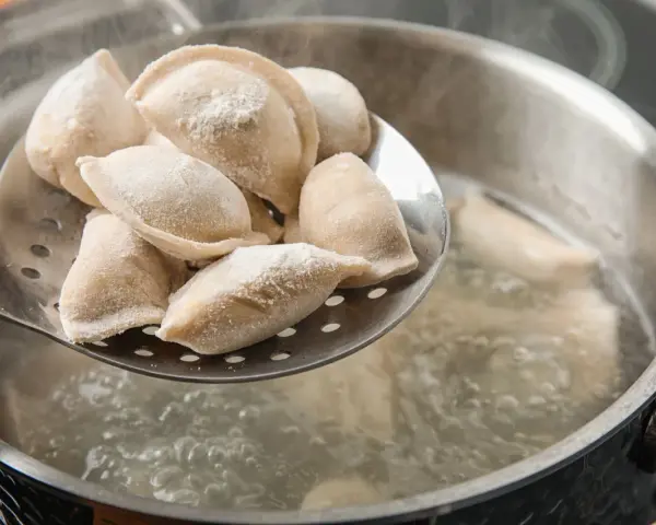 Gotowanie pierogów: na łyżce cedzakowej świeżo uformowane pierogi czekają na wrzucenie do wrzątku.