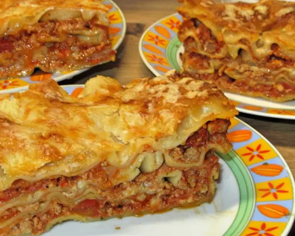 Prosty przepis na lasagne z mięsem mielonym. Aromatyczne, warstwowe danie z makaronem, sosem mięsnym i serem, podane na kolorowych talerzach.