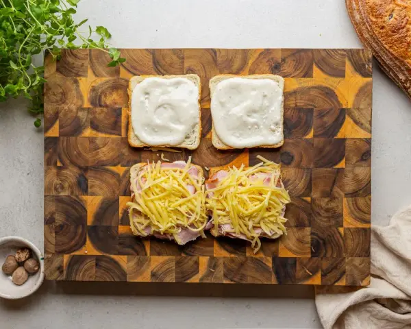 Przygotowanie croque madame: na kromkach chleba szynka i ser, na drugiej sos beszamelowy.
