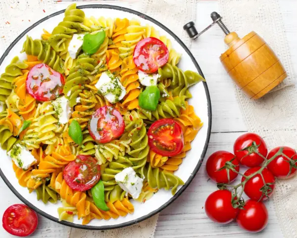 Kolorowy makaron z zielonego groszku, pomidorkami koktajlowymi i fetą, polany pesto.