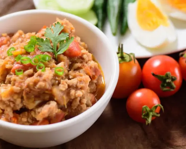 Pyszna pasta z makreli w pomidorach, udekorowana szczypiorkiem i natką. Obok świeże pomidorki i jajka na twardo.