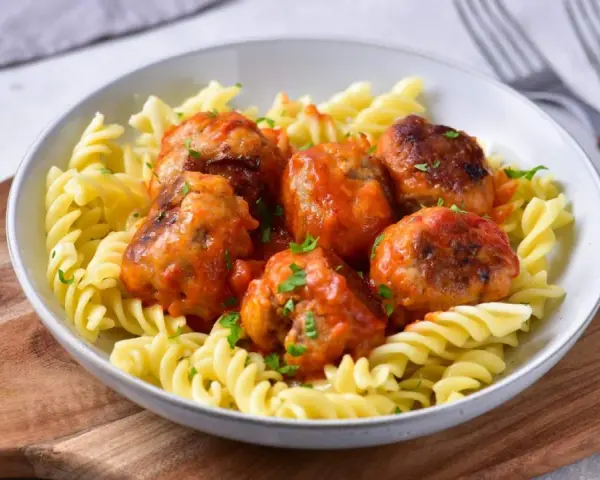 Pulpety w sosie pomidorowym jak u babci, podane z makaronem fusilli. Danie ozdobione posiekaną natką pietruszki.