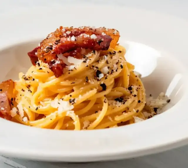 Spaghetti carbonara – przepis oryginalny ze śmietaną. Pyszne danie z makaronem, boczkiem i parmezanem, posypane świeżo mielonym pieprzem.