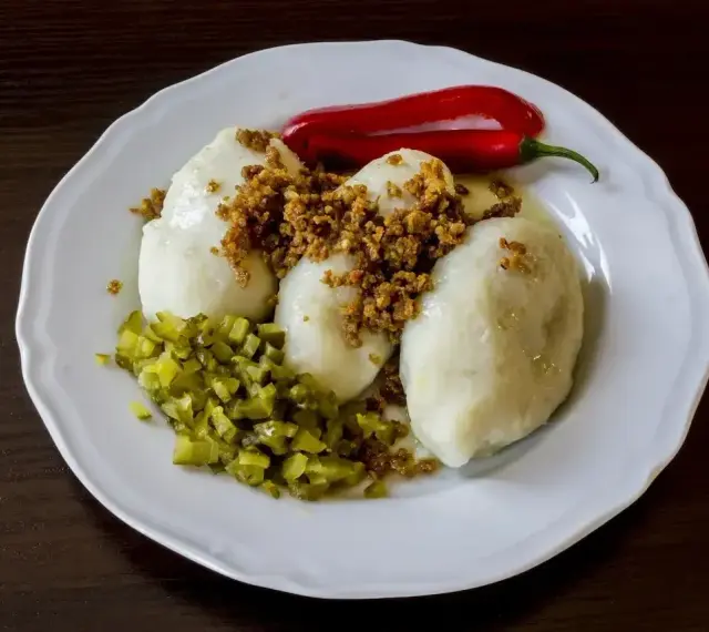 Trzy ziemniaczane kartacze z okrasą, posypane skwarkami, podane z ogórkiem kiszonym i papryczką chili.