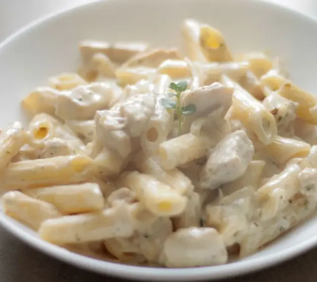 Penne z kurczakiem w kremowym sosie śmietanowo-serowym, udekorowane gałązką ziół. Pyszne danie obiadowe.