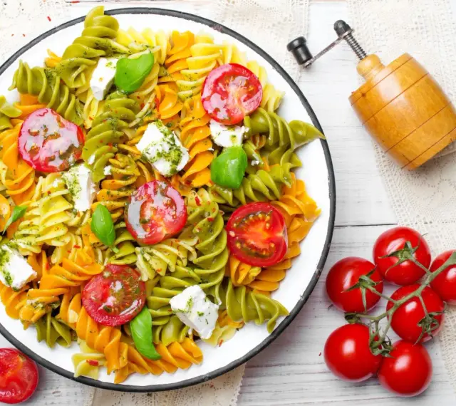 Kolorowy makaron z zielonego groszku, pomidorkami koktajlowymi i fetą, polany pesto.